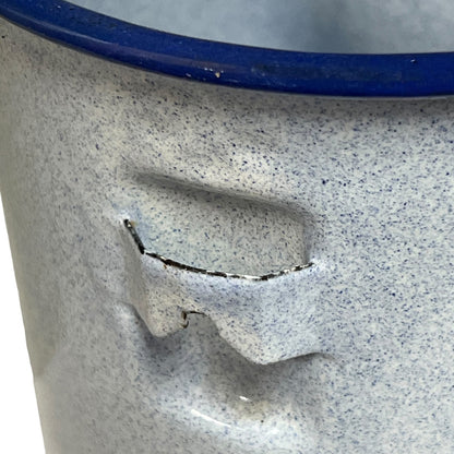 Close-up of a speckled light gray ceramic or enamel container with a dark blue rim and a small dark crack on the front.