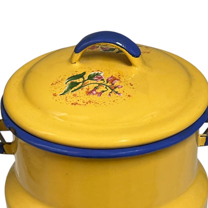 A yellow enamel lidded pot with a blue handle and rim, decorated with a small floral motif on the lid, shown against a plain white background.
