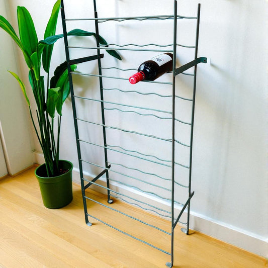 Vintage French wire wine rack with a bottle on a wooden floor next to a plant for sale from All Things French Store