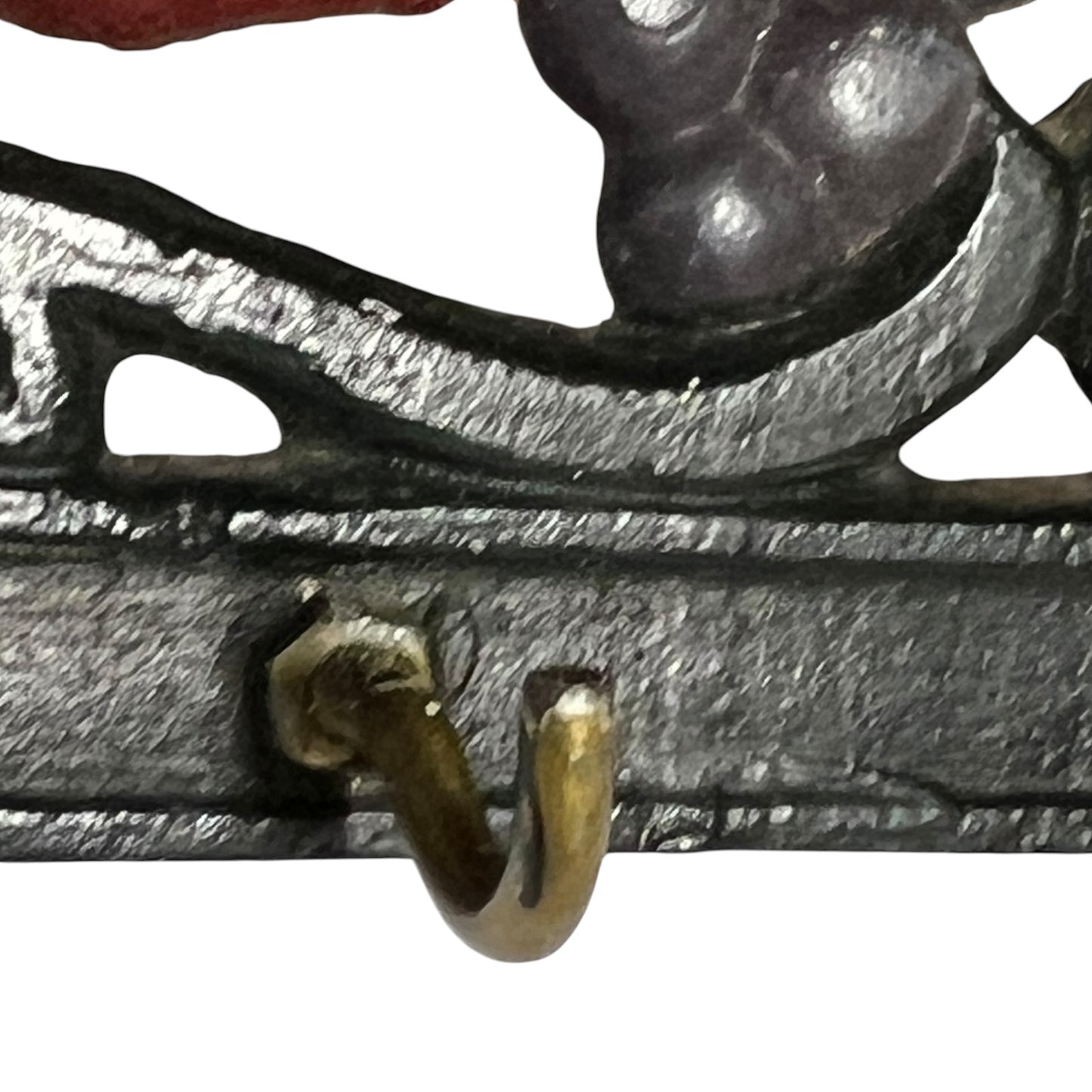 Close-up of a rustic cast iron wall hook with a textured dark gray finish and a small brass-toned hook, shown against a white background.
