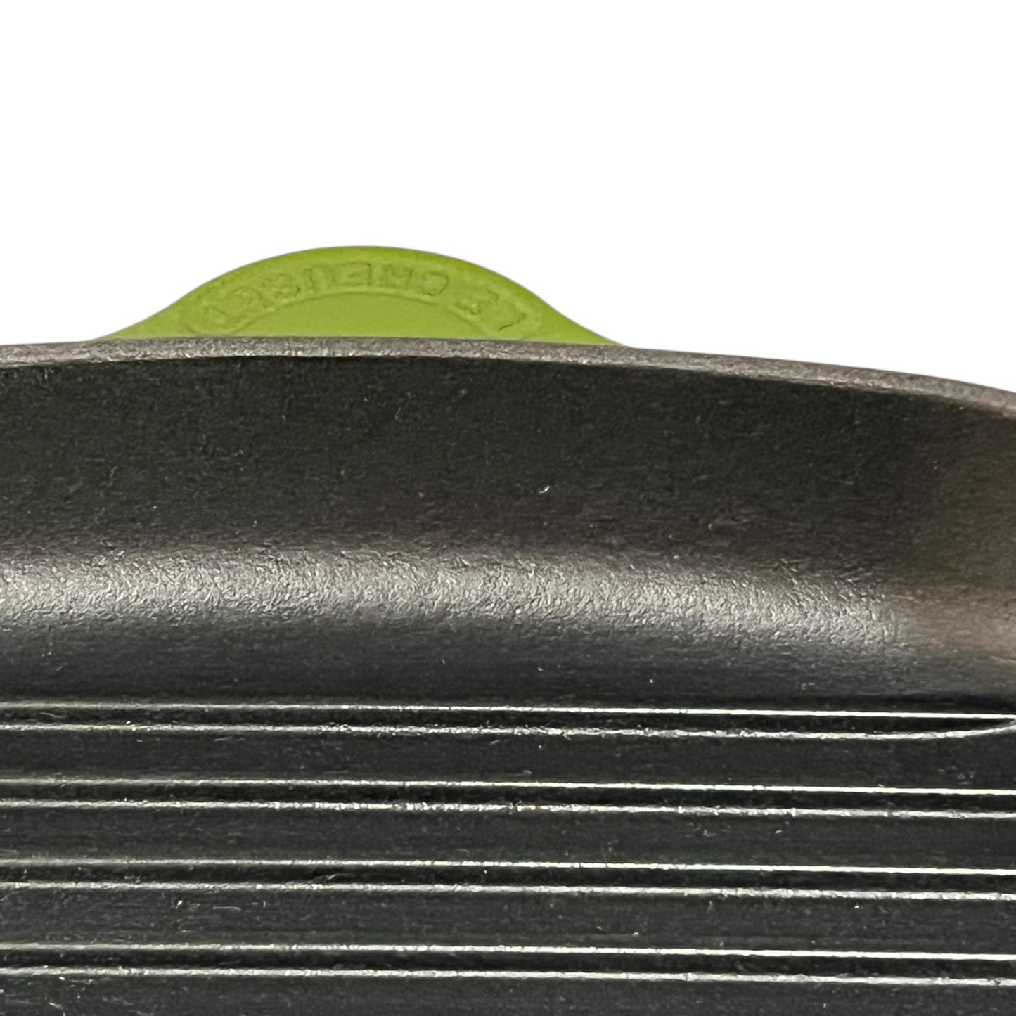 Close-up of a green cast iron skillet with a visible Le Creuset logo on a white background