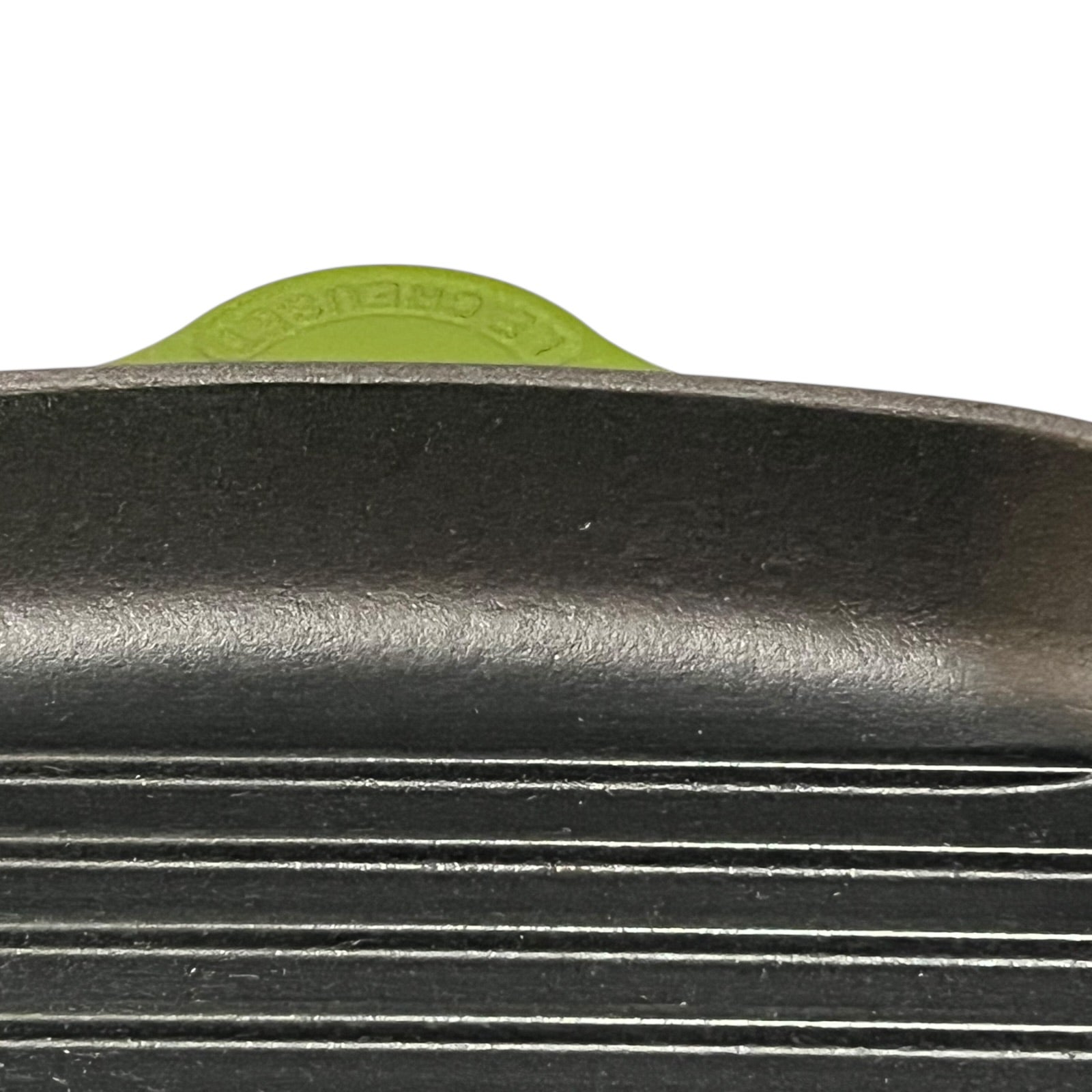 Close-up of a green cast iron skillet with a visible Le Creuset logo on a white background