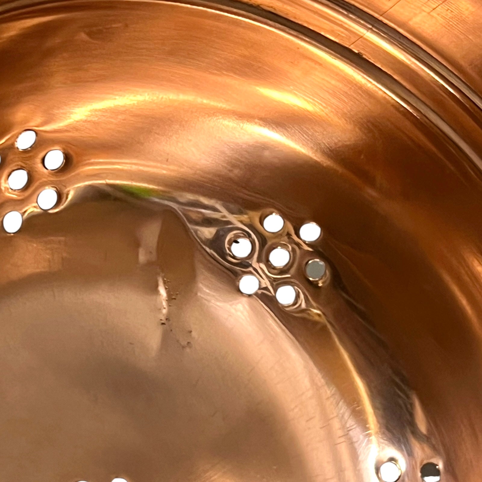 Close-up of the inside of a copper pot or pan with multiple small circular steam release valves or vents on the bottom.
