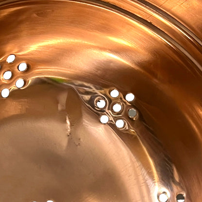 Close-up of the inside of a copper pot or pan with multiple small circular steam release valves or vents on the bottom.