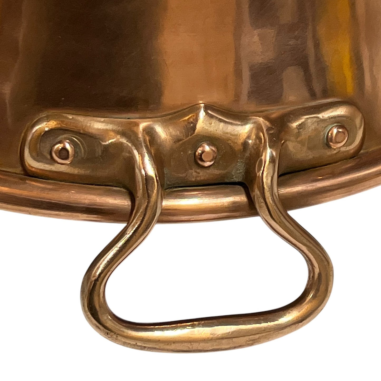 Close-up of a polished copper or brass pot handle attached with rivets, shown against a plain white background.