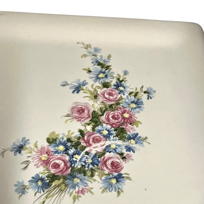 A close-up of a white ceramic surface featuring a vintage-style floral print with pink roses, blue daisies, and green leaves.