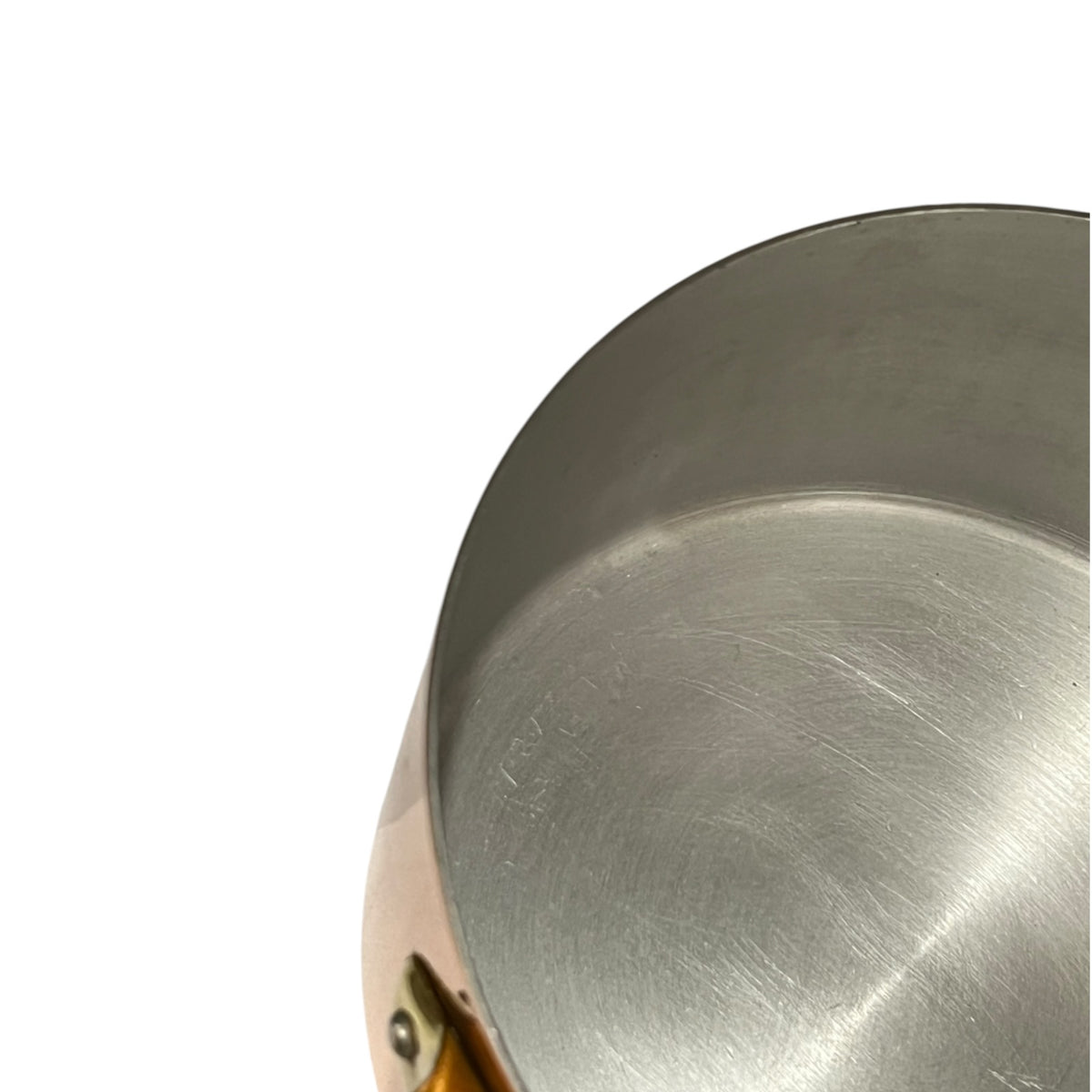 Close-up detail of a brushed copper pot or pan rim and interior, with a small portion of a copper-toned handle visible against a white background.