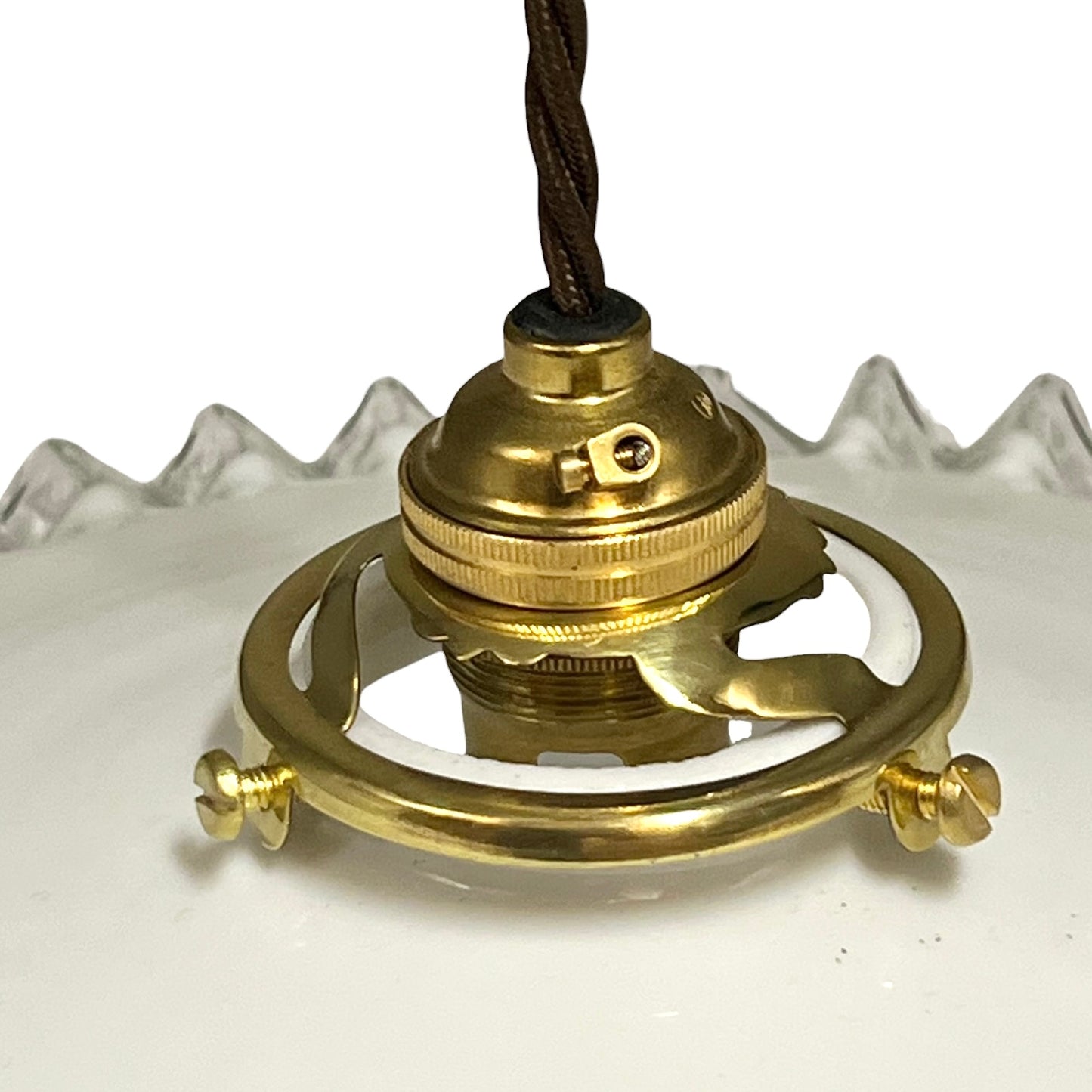 A close-up of a brass ceiling light fixture canopy and mounting ring with a dark brown fabric cord, resting on a white surface.