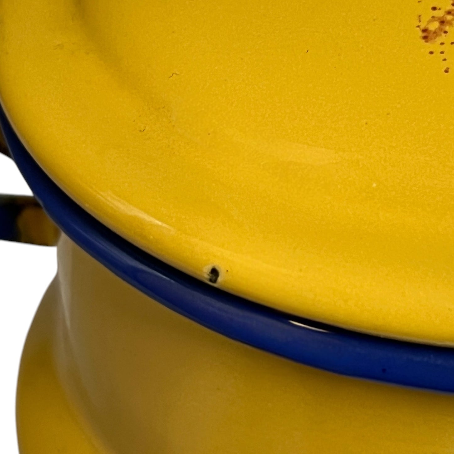 Close-up of a yellow enamel pot or container with a blue rim and a small dark defect near the edge.