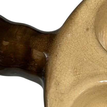 Close-up of a ceramic dish with a glossy brown handle and a beige glazed body showing fine crackle lines, set against a plain white background.