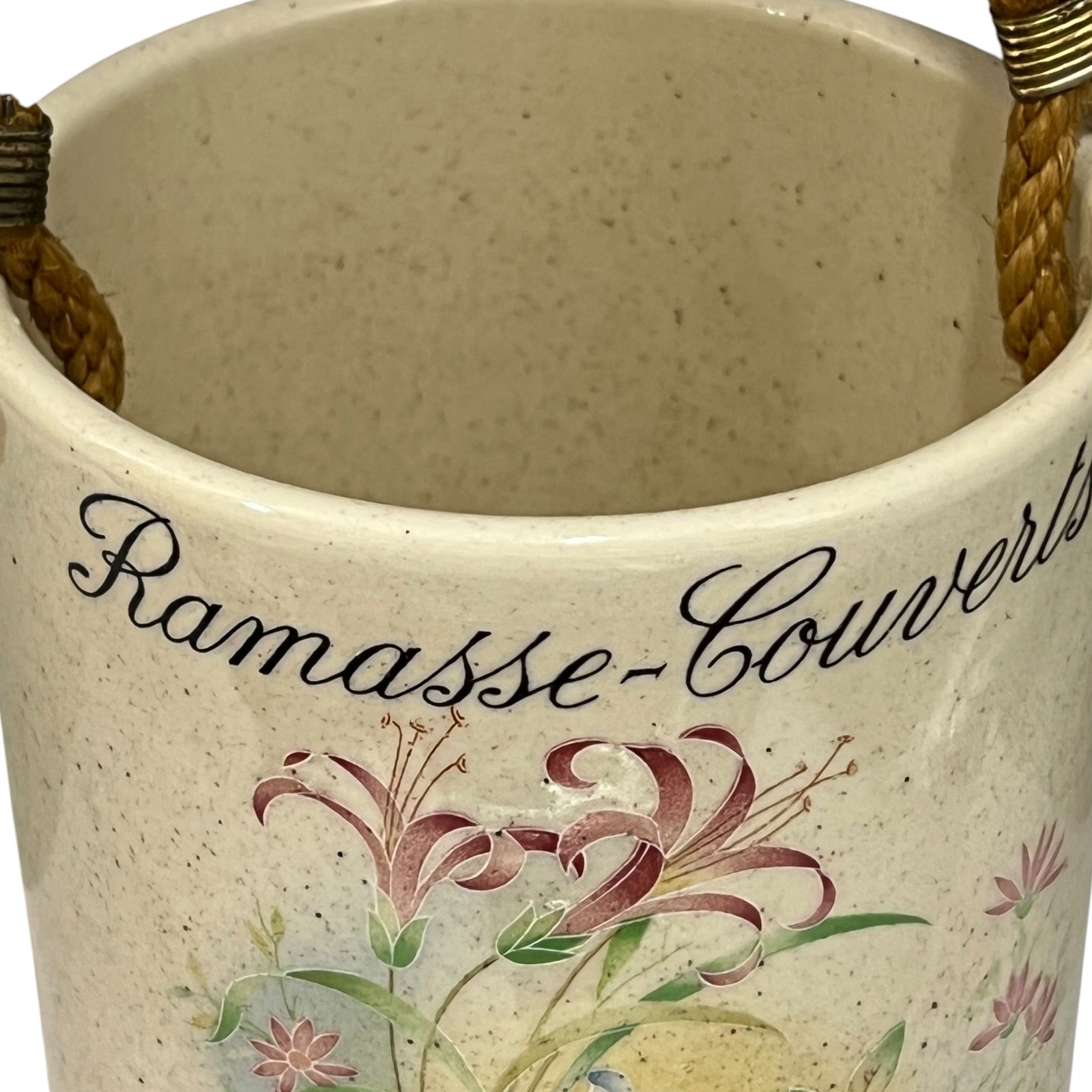 Close-up of a speckled cream ceramic pot with rope handles and a floral print featuring lilies and the text 'Ramasse-Couverture'.