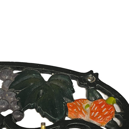 Close-up of a decorative cast iron hook set or stand featuring a black metal frame with embossed grape leaves and orange-red grapes, shown against a plain white background.