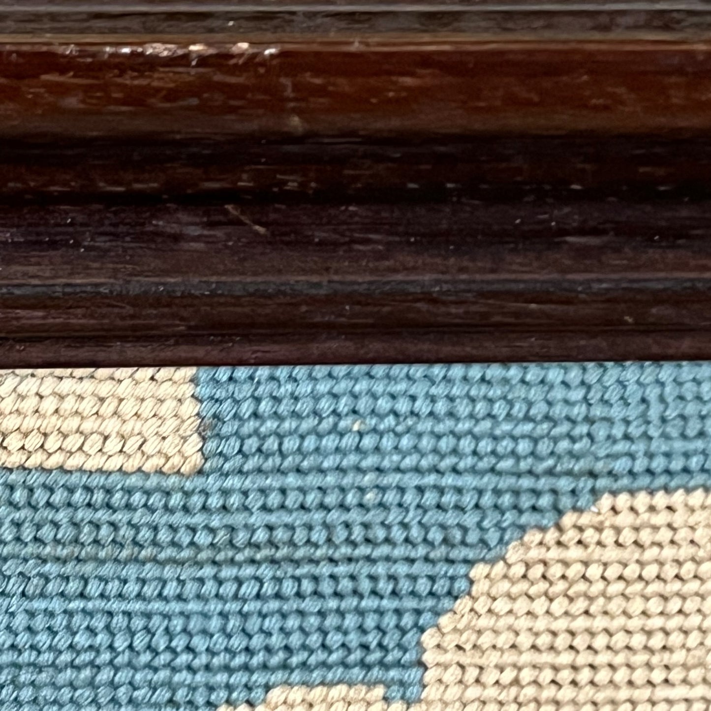 Close-up of a woven textile with a blue and beige geometric pattern, shown beneath a dark brown wooden surface.