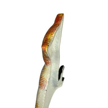 A close-up of a decorative object with a white base and textured orange, yellow, and red painted details, shown against a plain white background.