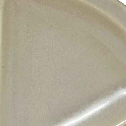 A close-up of a light beige ceramic surface, likely a plate or dish, showing a slightly textured glaze with a bright reflection along the bottom right edge.