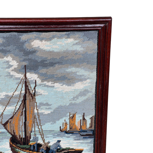 Framed needlepoint of a maritime scene with ships and clouds.