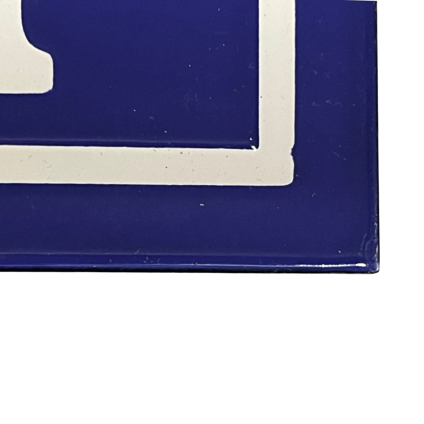 A close-up of a glossy dark blue plaque with a white corner border and partial white graphic detail, shown against a white background.
