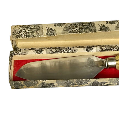 A vintage metal cake slice with a deer hoof handle, presented inside an open patterned box with a red interior lining