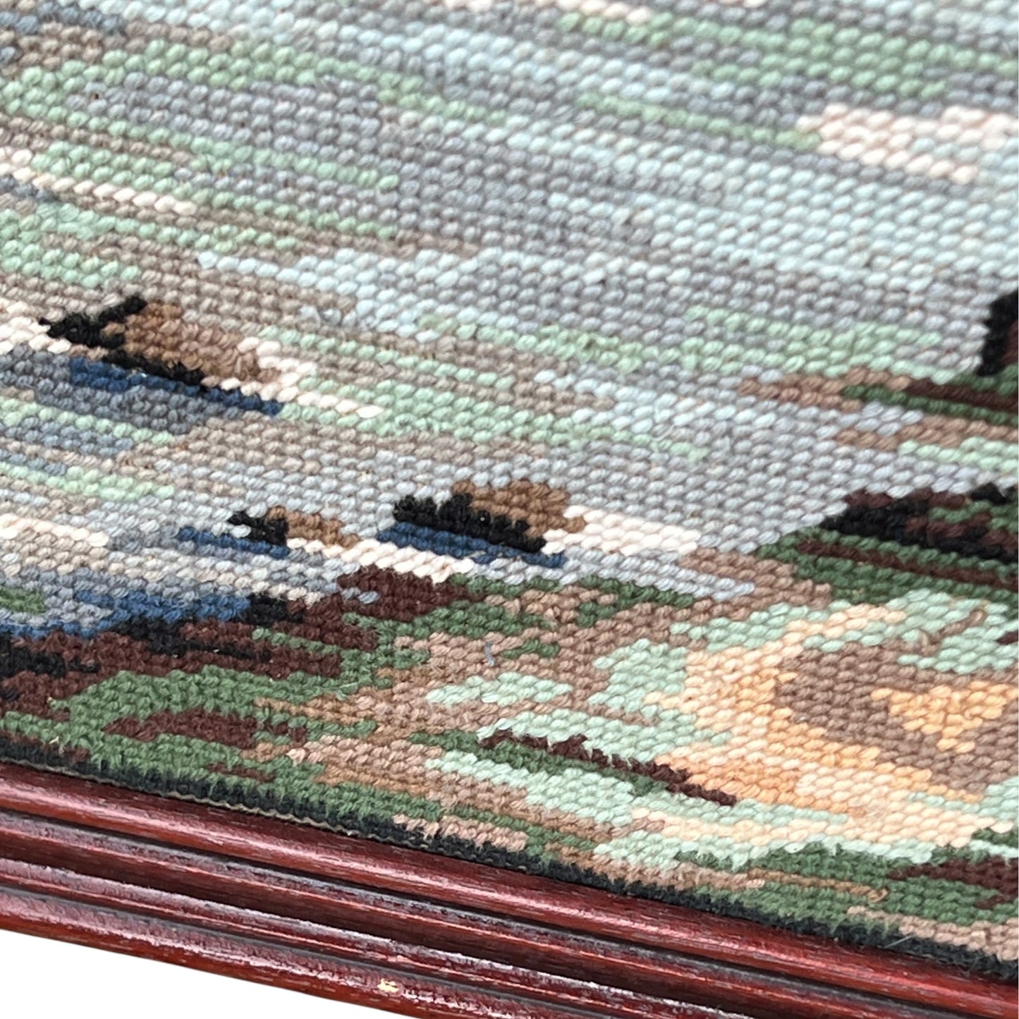 Close up of framed tapestry needlepoint with a coastal scene and wooden frame on a white background