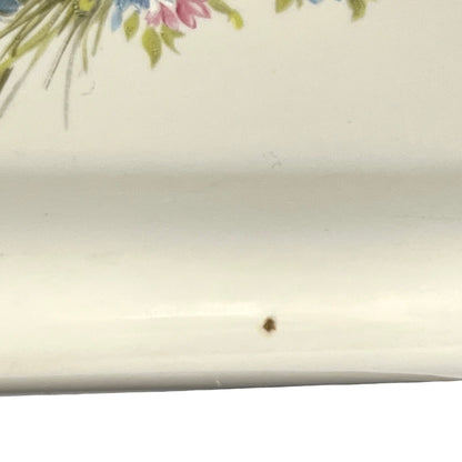 Close-up of a white ceramic surface with a small brown speckle near the bottom center and part of a floral print visible at the top edge.