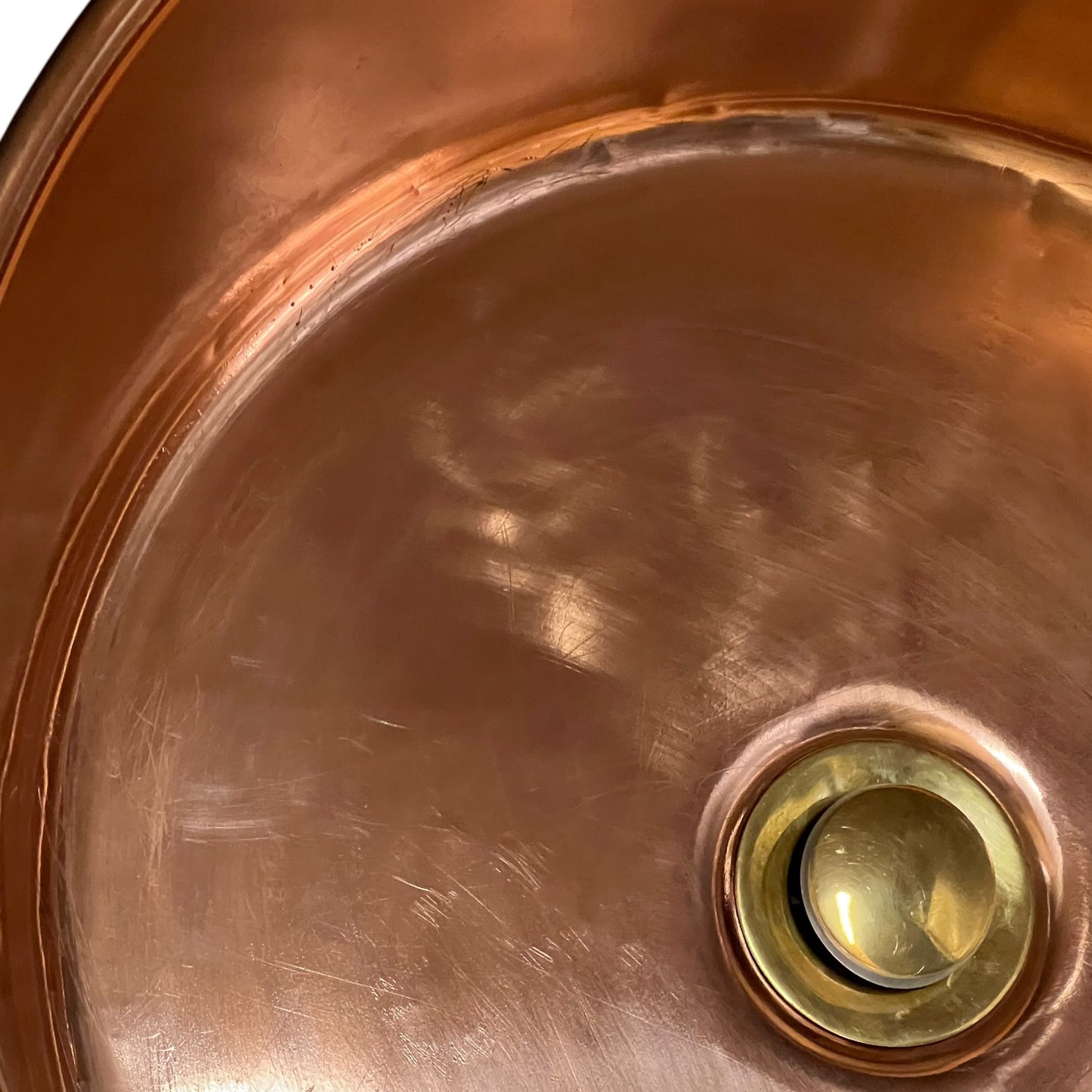 Close-up of a copper sink basin with a brass drain, showing the brushed metal surface and reflective finish.