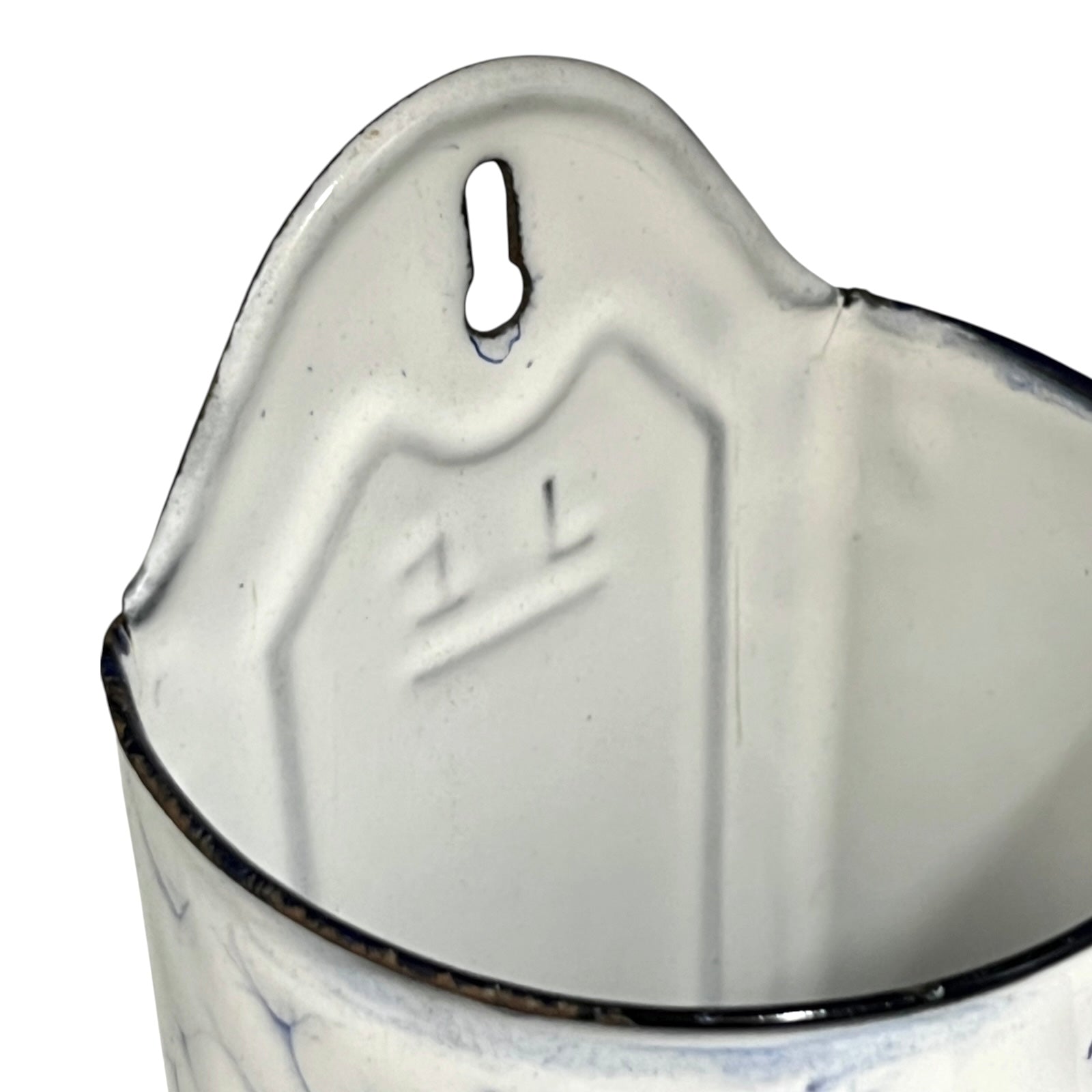 Close-up of the interior of a white enamel jug with a blue floral pattern and a dark rim, showing the embossed lettering and a hanging hole at the top.