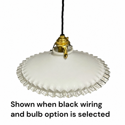 A vintage-style white glass pendant light with a scalloped edge and a gold-toned metal fixture, suspended by a black cord against a white background. Text at the bottom reads, 'Shown when black wiring and bulb option is selected.