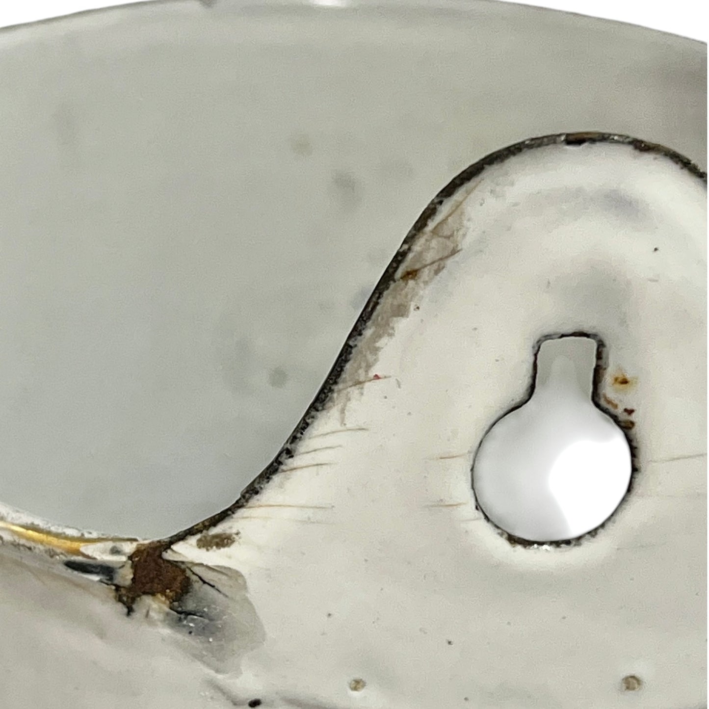 Close-up of a white planter with a small rounded recessed detail and dark chipped edges, photographed against a matching light background