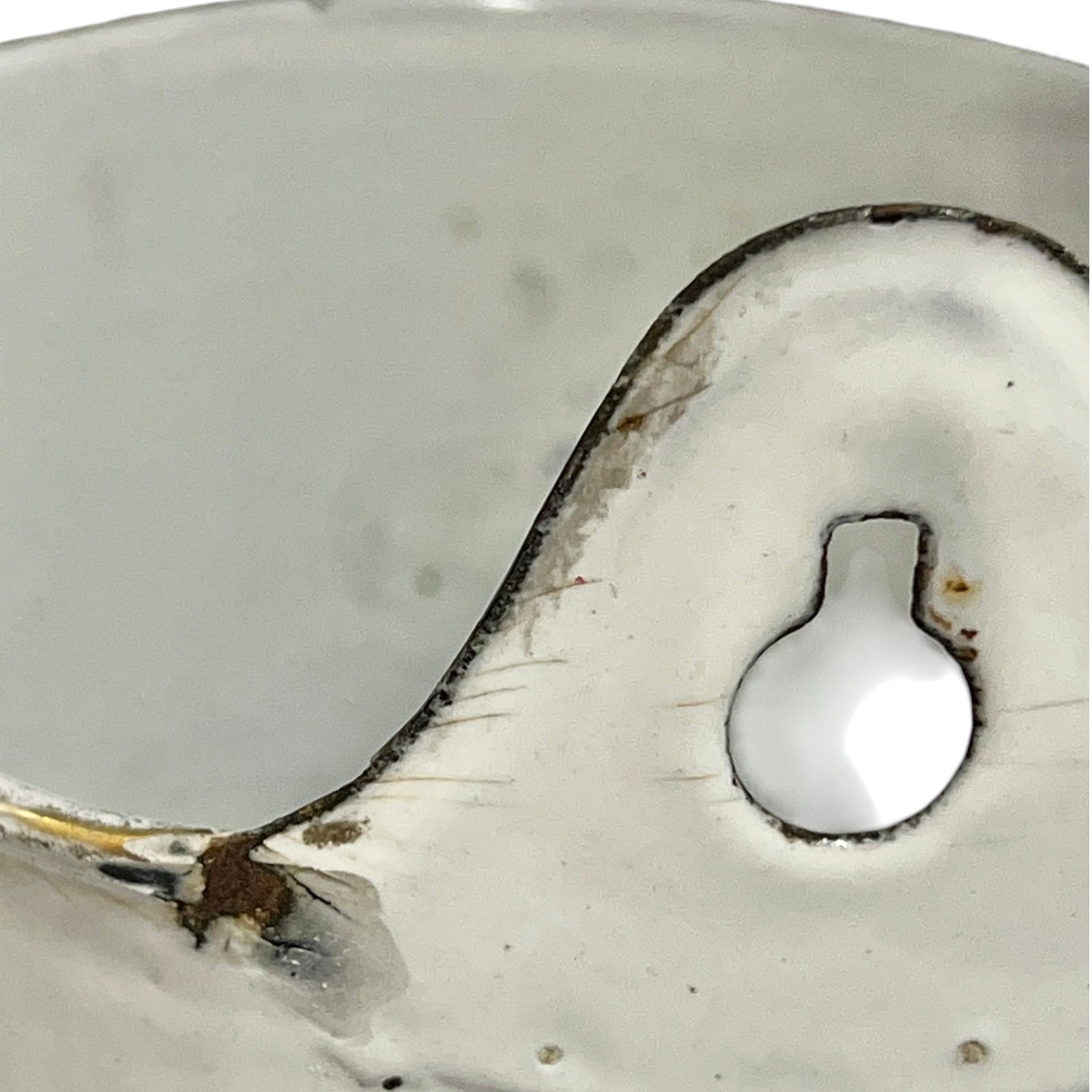 Close-up of a white planter with a small rounded recessed detail and dark chipped edges, photographed against a matching light background