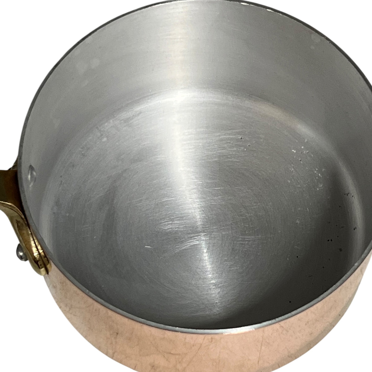 A close-up top-down view of a copper and stainless steel saucepan with a brass handle, isolated on a white background.
