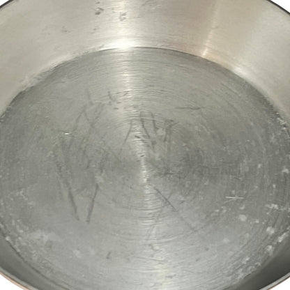 A close-up view of the inside of a brushed stainless steel pot or pan, showing visible scratches and wear on the bottom surface.