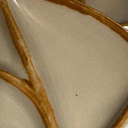 Close-up of a ceramic plate with a textured beige surface and a thick, rustic brown branch-like glaze design.