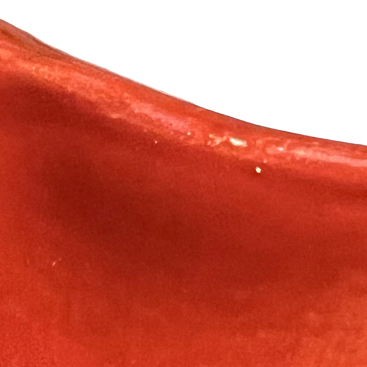 A close-up of a glossy red curved surface, likely a ceramic bowl, vase, or decorative vessel, against a plain white background.