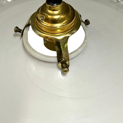 A close-up of a vintage brass ceiling light fixture canopy with a white porcelain shield and mounting screws, set against a white background.