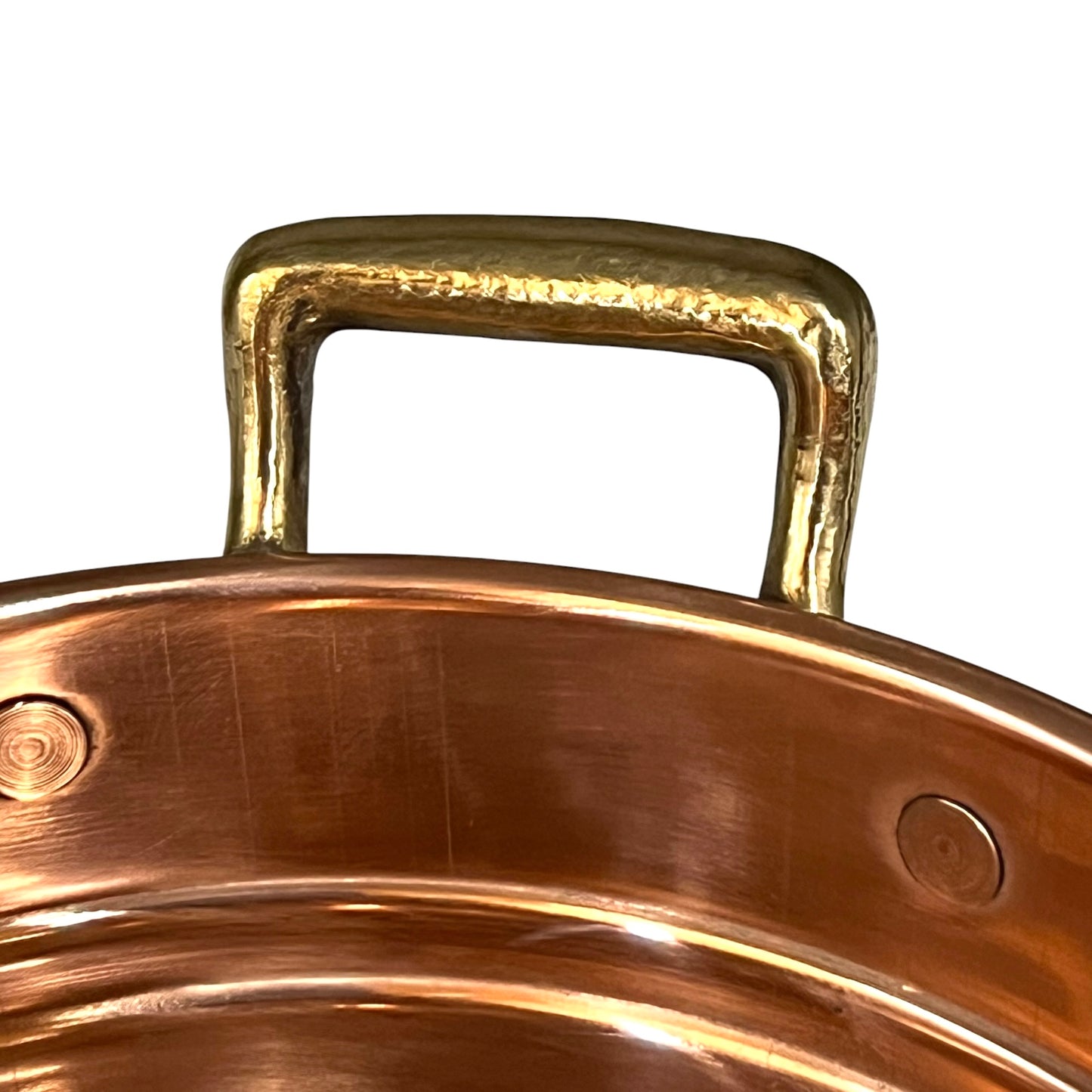 Close-up of a hammered brass pot handle attached to a copper-colored metal pot rim, shown against a plain white background.