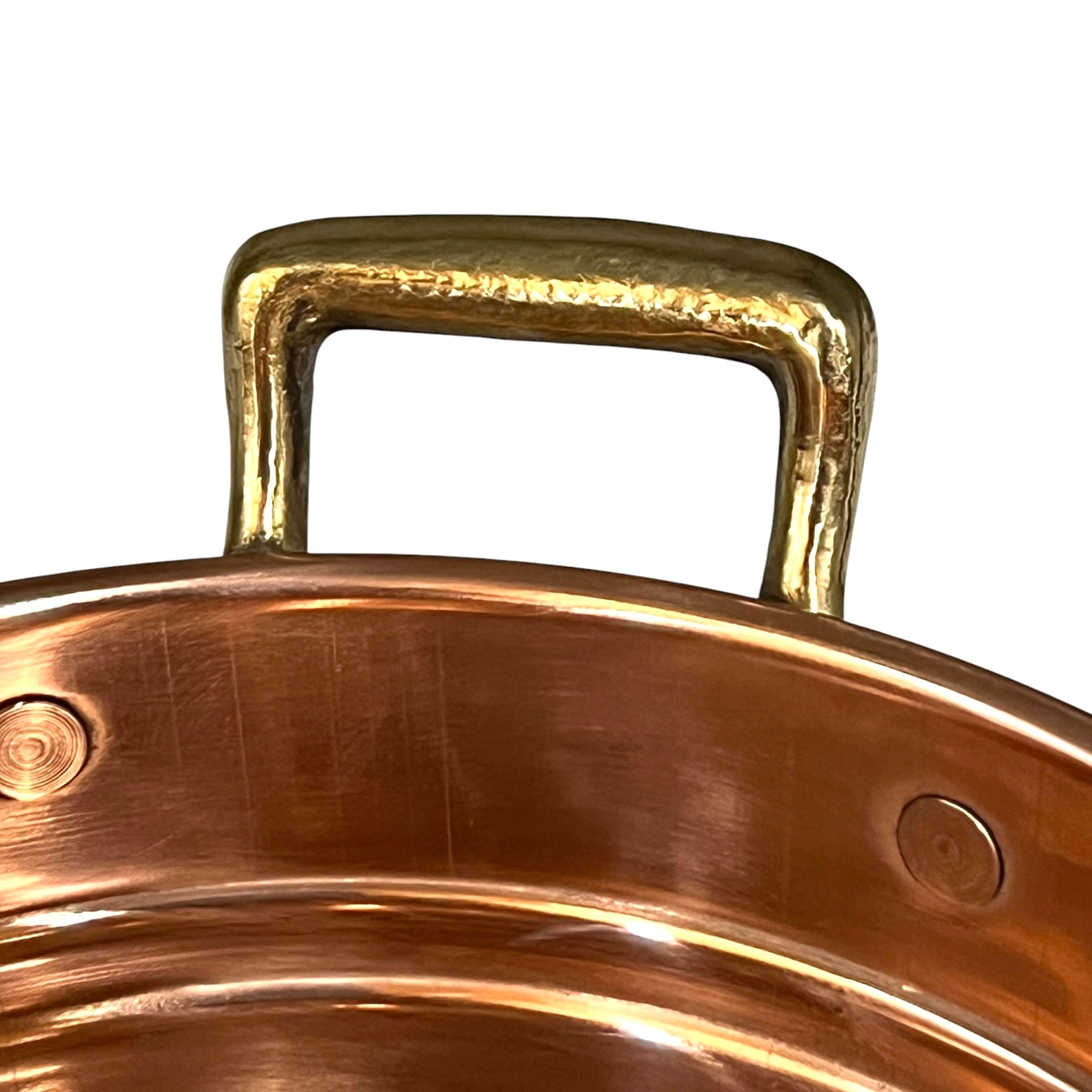 Close-up of a hammered brass pot handle attached to a copper-colored metal pot rim, shown against a plain white background.