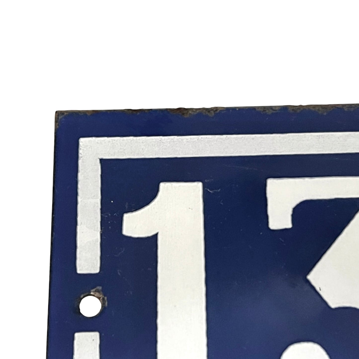 Close-up of a blue and white enamel-style sign showing part of the number 133 with a small round hole near the lower left and a worn, rusted edge along the top.