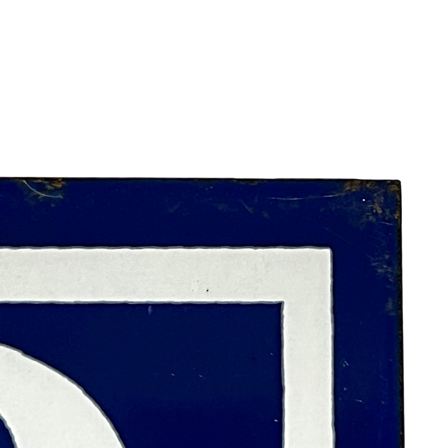 Close-up of a dark blue sign or plaque with a white border and part of a white curved shape visible, photographed against a white background.