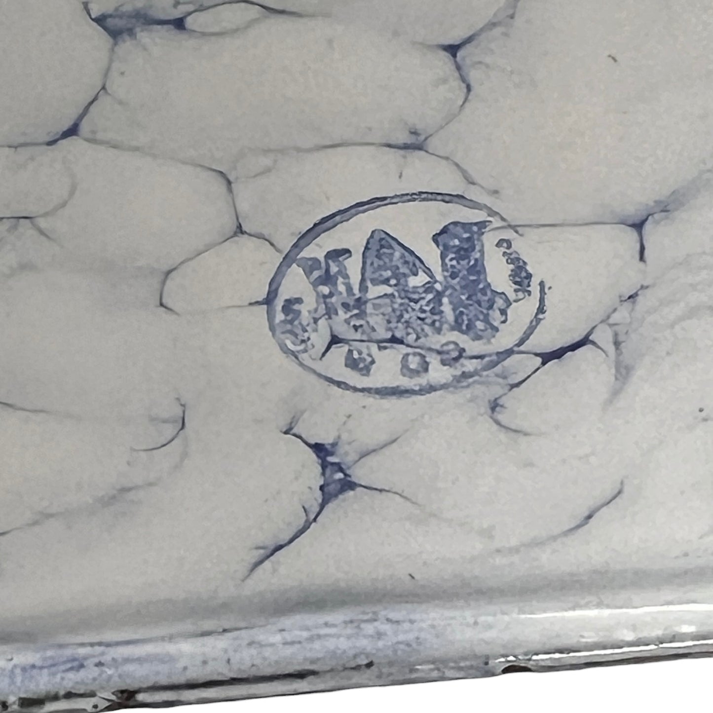 Close-up of a white enamel surface with blue crackle glaze lines and a blue oval maker's mark stamp in the center.