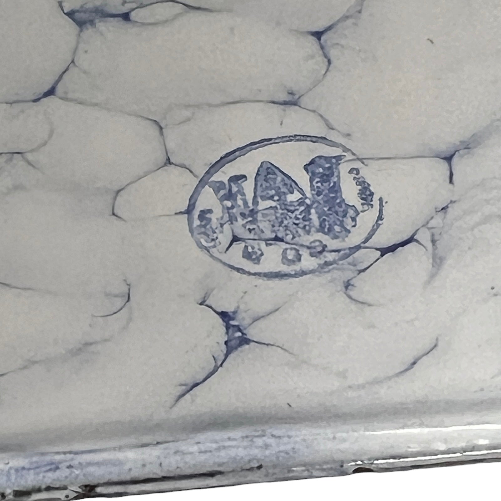 Close-up of a white enamel surface with blue crackle glaze lines and a blue oval maker's mark stamp in the center.