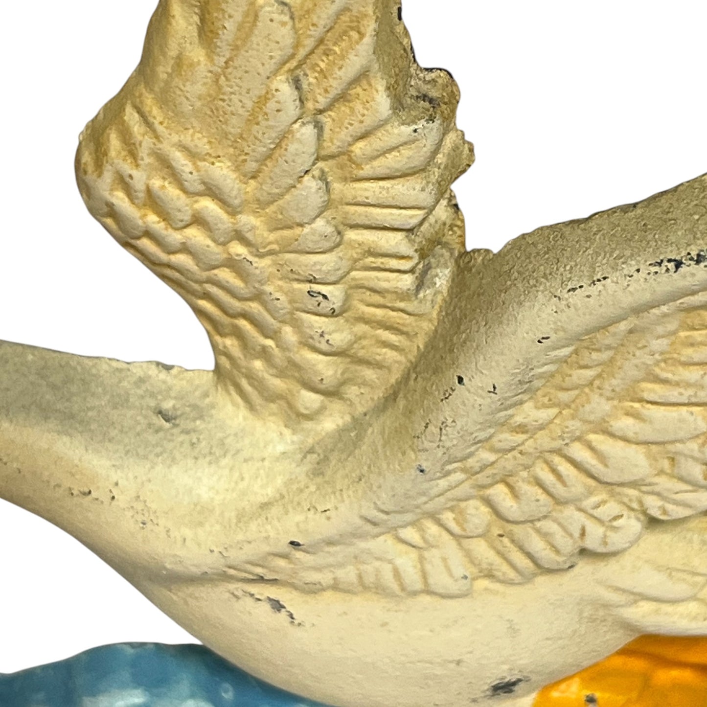 Close-up detail of a textured bird figurine, showing carved wing and body details in a weathered cream-beige finish with small dark specks, against a white background.
