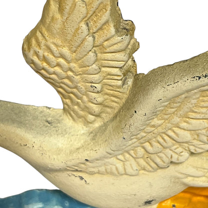 Close-up detail of a textured bird figurine, showing carved wing and body details in a weathered cream-beige finish with small dark specks, against a white background.