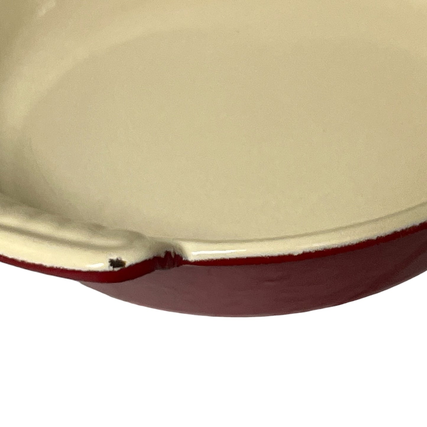 Close-up of a round cast iron skillet showing the cream-colored enamel interior and the dark red exterior rim against a white background.