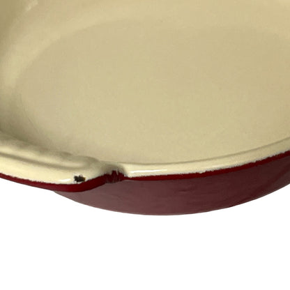 Close-up of a round cast iron skillet showing the cream-colored enamel interior and the dark red exterior rim against a white background.