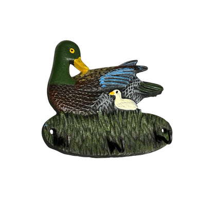 A decorative duck figurine featuring a large green-and-brown mallard with blue wing feathers and a small white duckling, mounted on a grass-textured base against a plain white background.