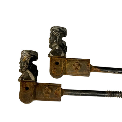 Two antique metal shutter dogs with sculpted bust-shaped tops, shown on a plain white background.