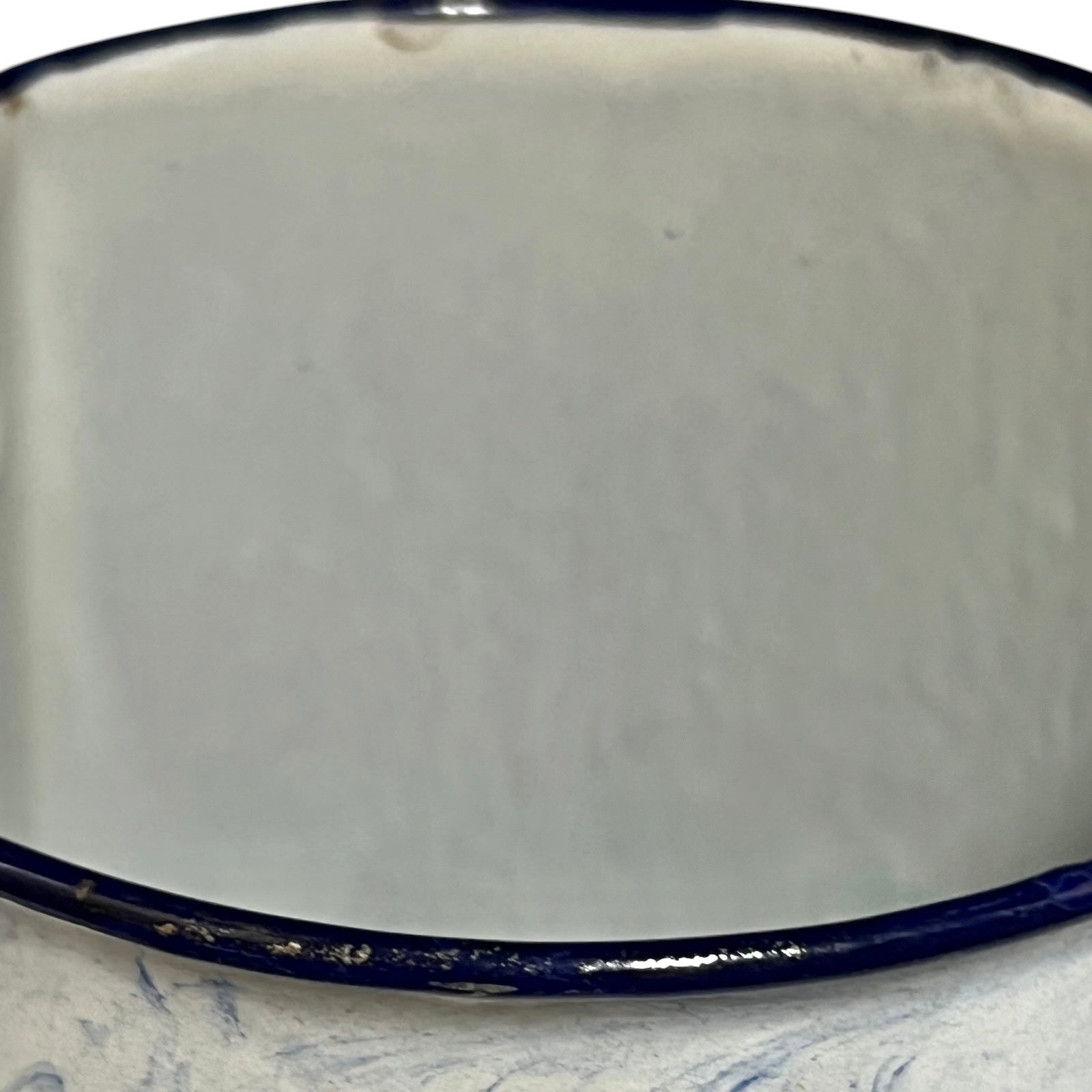 Close-up of an enamel pot with a glossy off-white interior and a dark navy blue rim, resting on a light blue marbled surface.