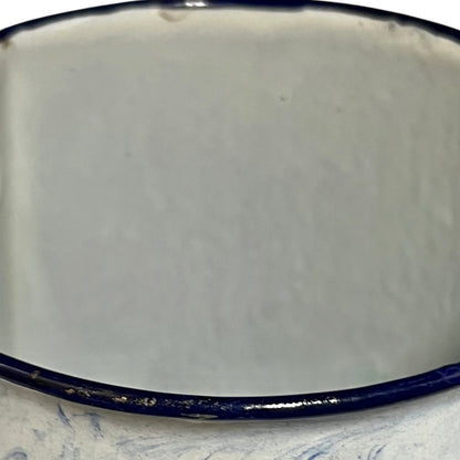 Close-up of an enamel pot with a glossy off-white interior and a dark navy blue rim, resting on a light blue marbled surface.