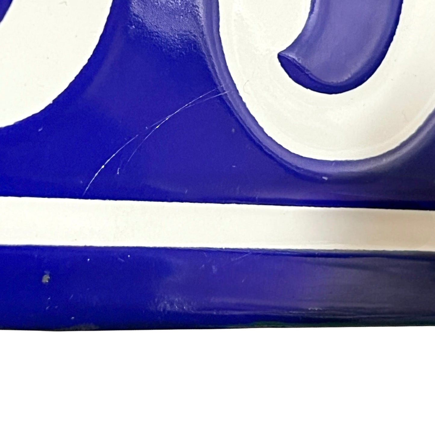 Close-up of a glossy blue and white decorative surface with curved white lettering or scrollwork and a horizontal white stripe.