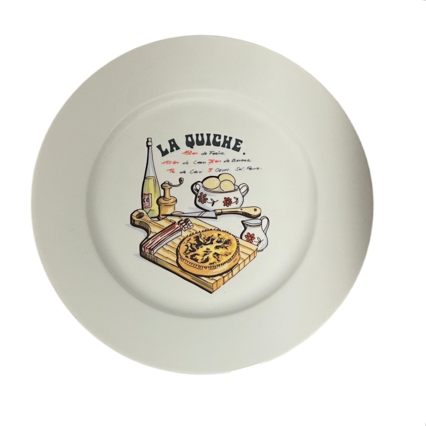 White plate with 'La Quiche' illustration featuring a pie, eggs, and other kitchen items on a white background.